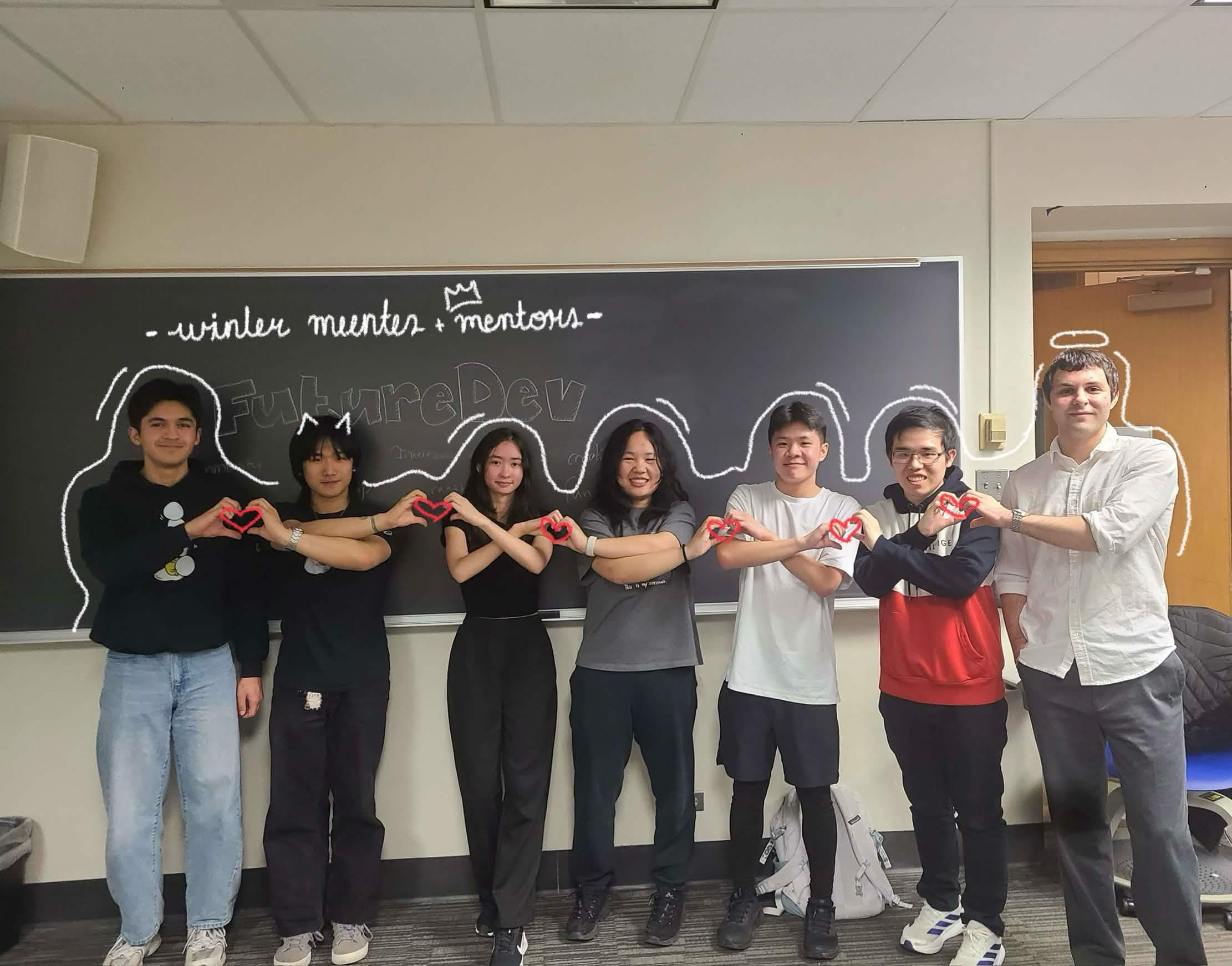 FutureDev mentees and mentors making heart hands together in front of a classroom chalkboard